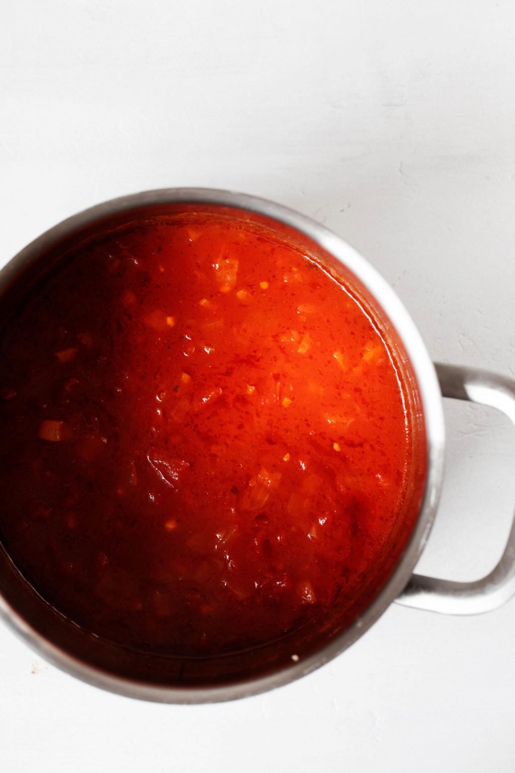 A large, silver pot is filled with a recently simmered batch of bright red, tomato soup.