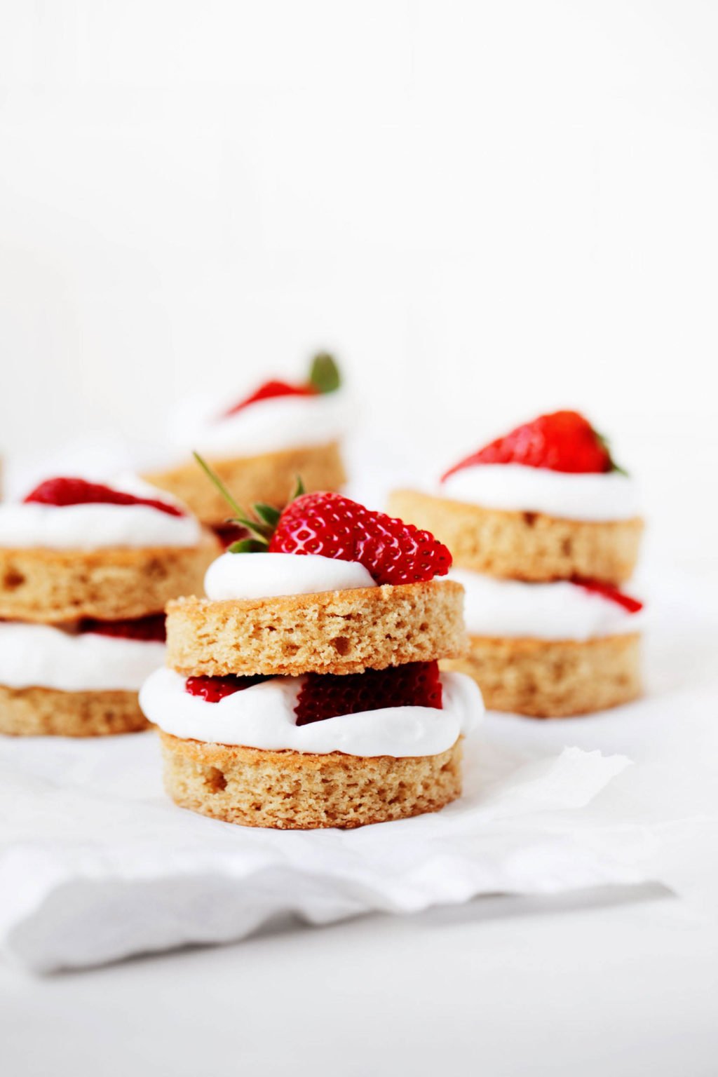 Four vanilla cakes have been stuffed with strawberries and cream. They're resting on a white sheet of crumpled parchment paper.