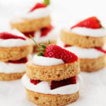 Four stacks of vegan strawberry shortcake are lined up on a sheet of white parchment paper.