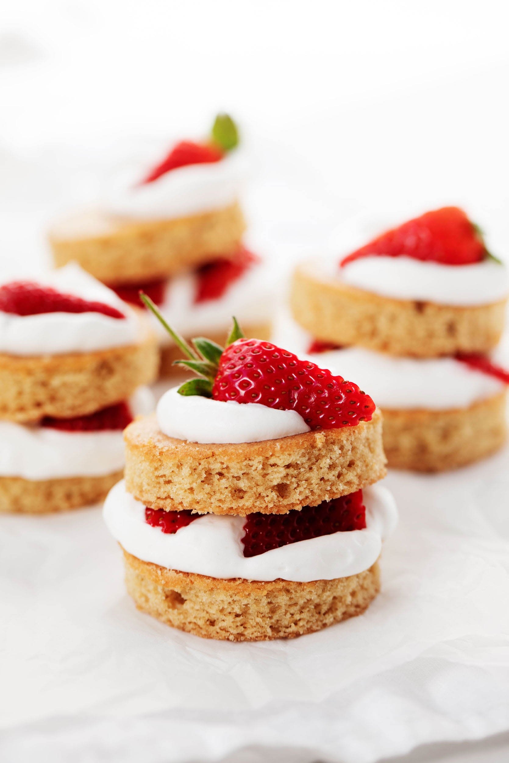 Four stacks of vegan strawberry shortcake are lined up on a sheet of white parchment paper.