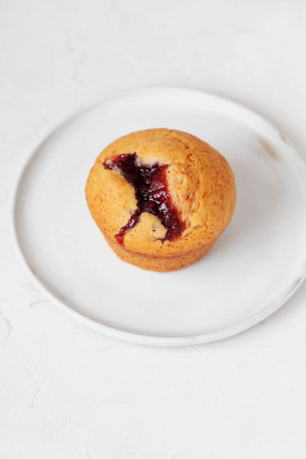 A vegan baked good with raspberry preserves is resting on a small white dessert plate.