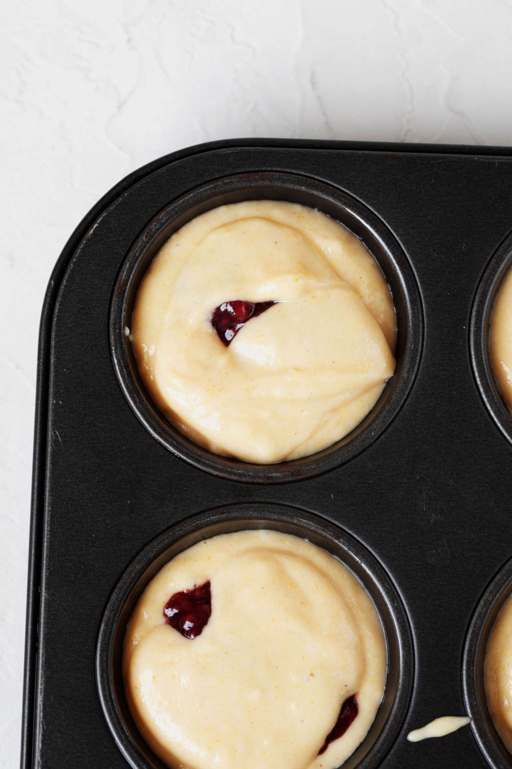 An overhead image of batter that has been poured into a black muffin pan.