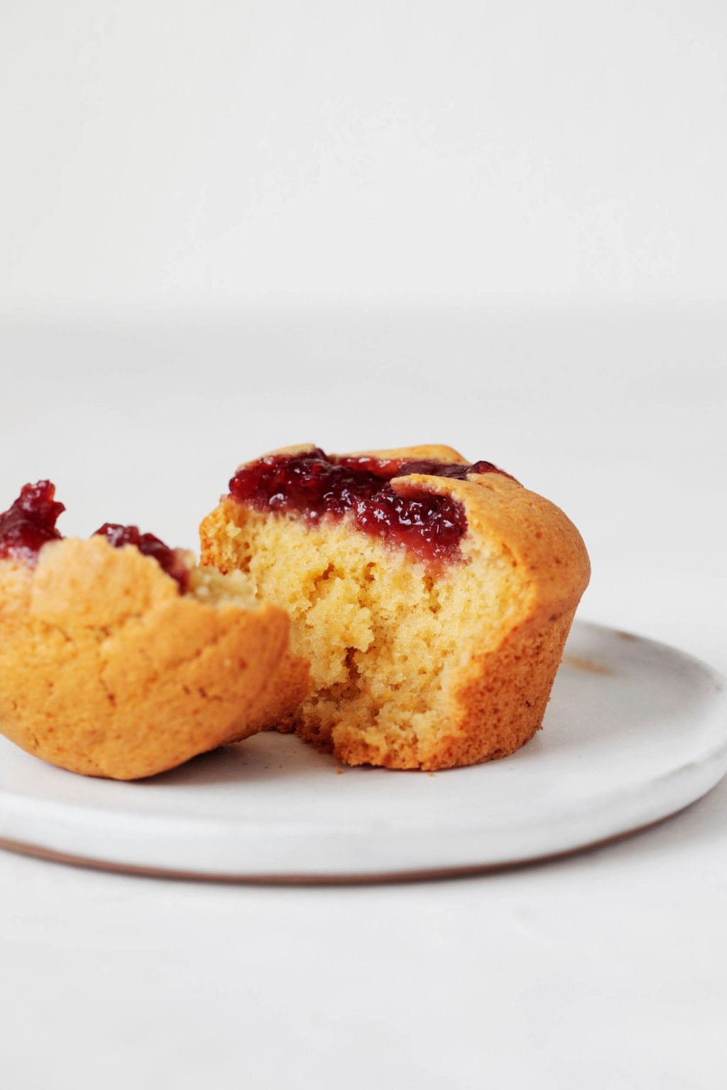 A vegan corn and jam muffin is resting on a small, white plate.