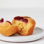 A vegan corn and jam muffin is resting on a small, white plate.