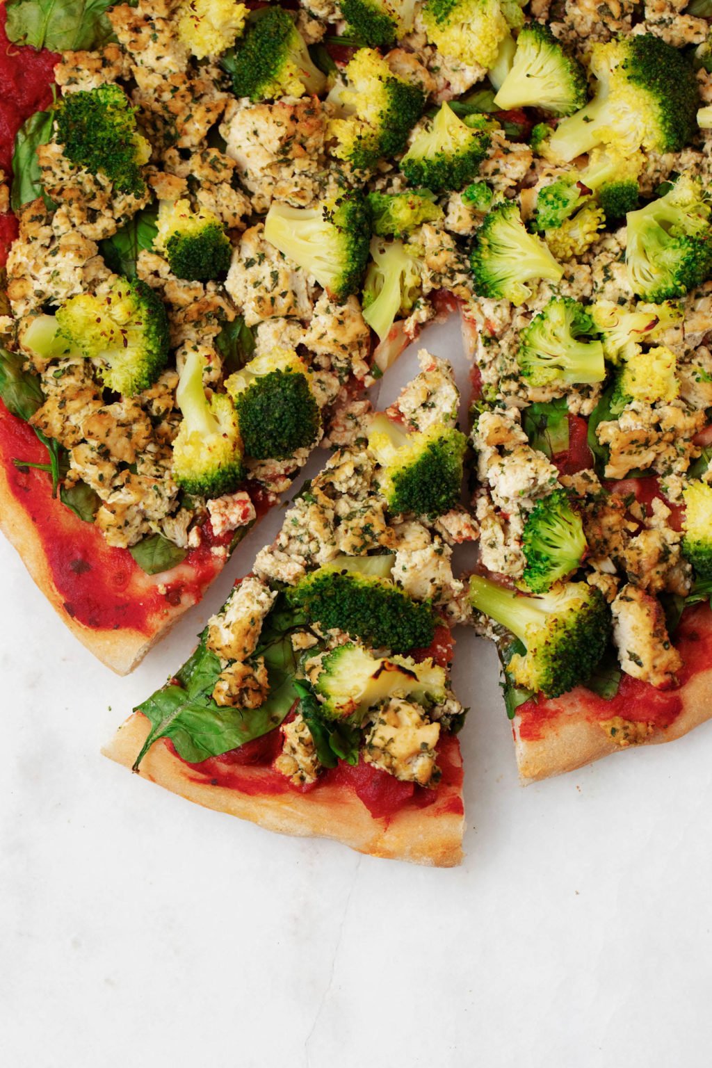A slice of pizza has been cut out of a round pie. The pizza is topped with green vegetables and tofu.