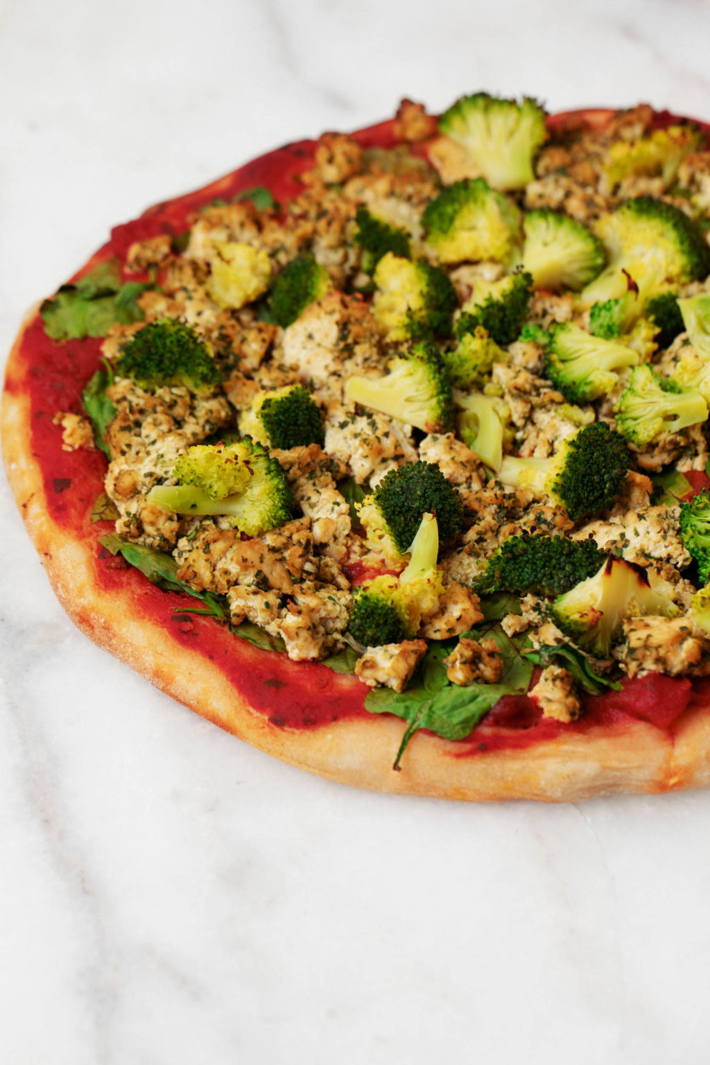 A plant-based green goodness pizza is topped with vegetables and herbs. It's perched on a marble surface.