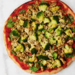 A vegan pizza made with herbed tofu and green vegetables rests on a marble surface.