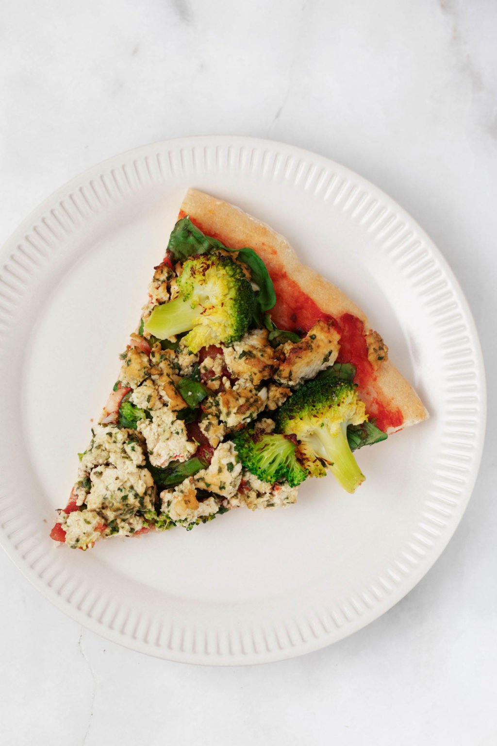 A slice of vegan flatbread is topped with vegetables and tofu.