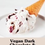 A small, round white plate holds an ice cream sugar cone with a scoop of cherry ice cream.
