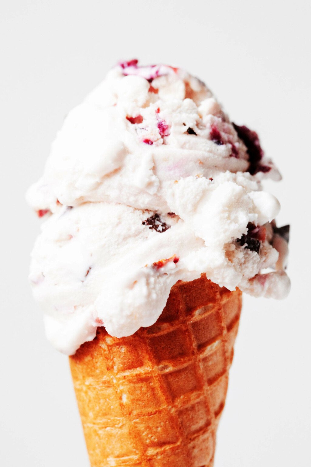 A brown sugar cone is holding a scoop of light pink chocolate cherry ice cream.