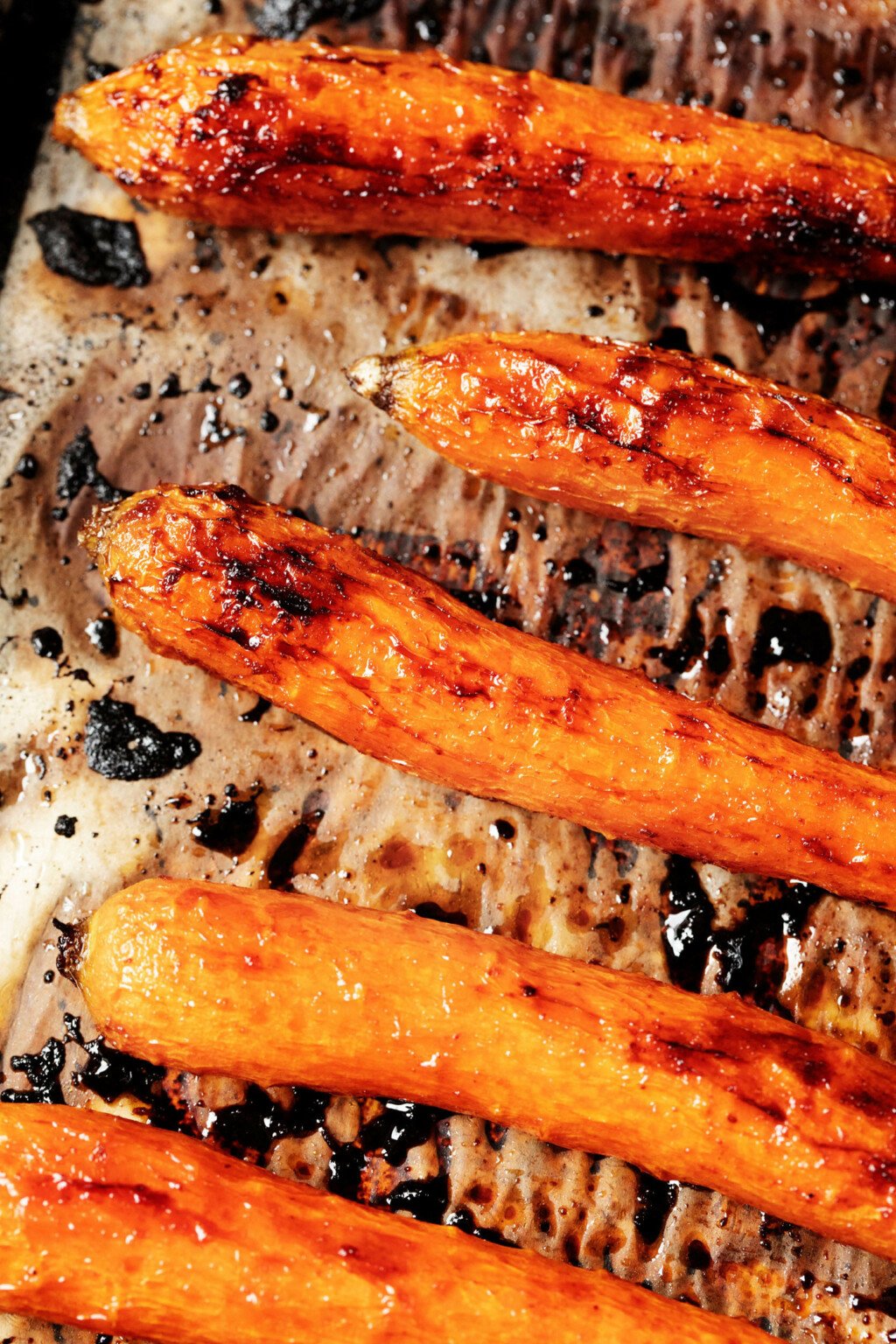 Roasted carrots are resting on a parchment-lined baking sheet.