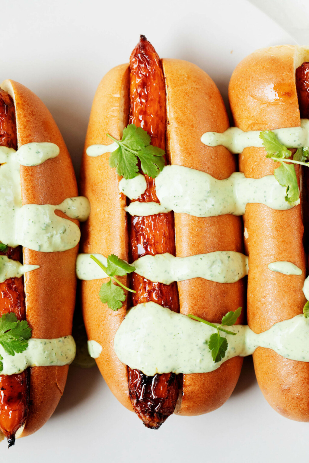 Glazed carrot dogs have been piled into buns and topped with a green dressing.