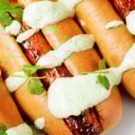 Light brown buns have been filled with glazed, roasted root vegetables. They're topped with green sauce and some fresh herbs.