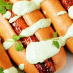 Light brown buns have been filled with glazed, roasted root vegetables. They're topped with green sauce and some fresh herbs.