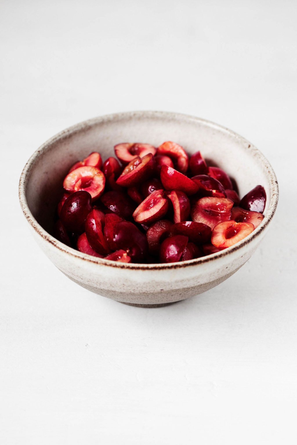A white, ceramic bowl is resting on a white surface. It contains bright red, fresh fruit.