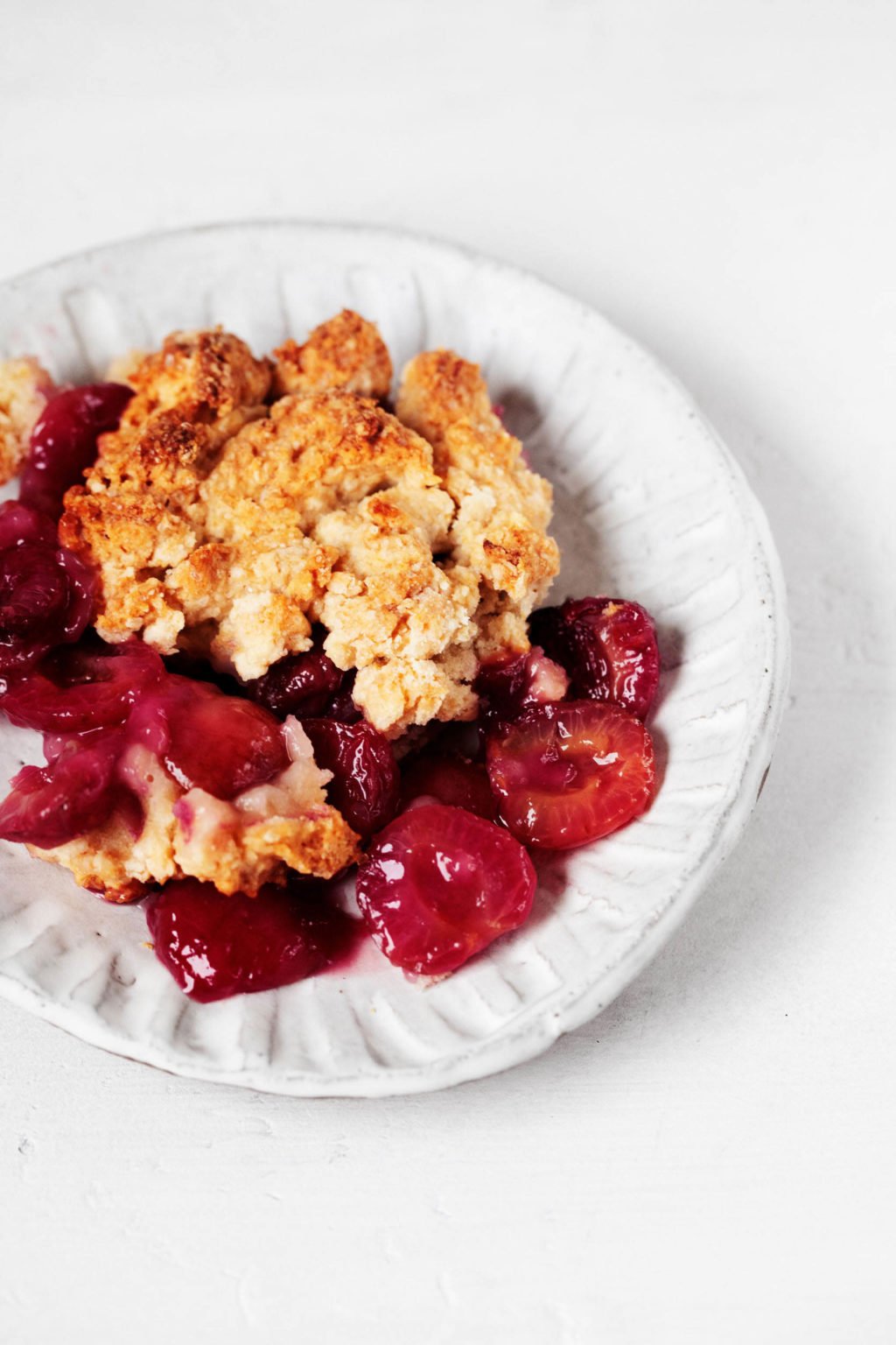 An angled photo of vegan cherry cobbler, which has been piled onto a small, white dessert plate.