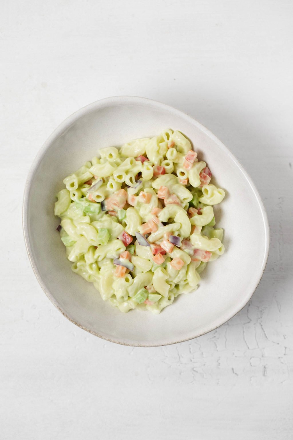 A asymmetrical white bowl holds a creamy vegan pasta salad.