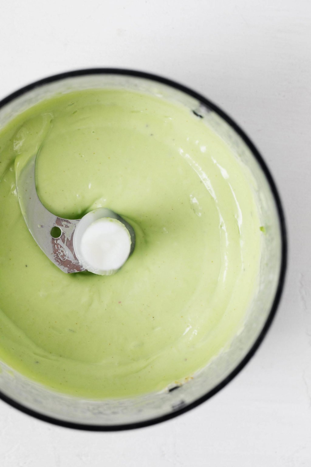 A light green sauce is being blended in a food processor.