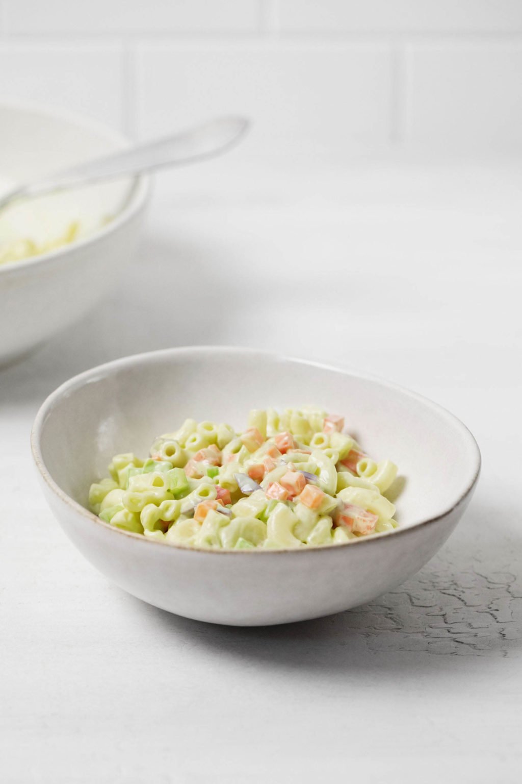Two bowls of a creamy vegan pasta salad rest on a white surface.
