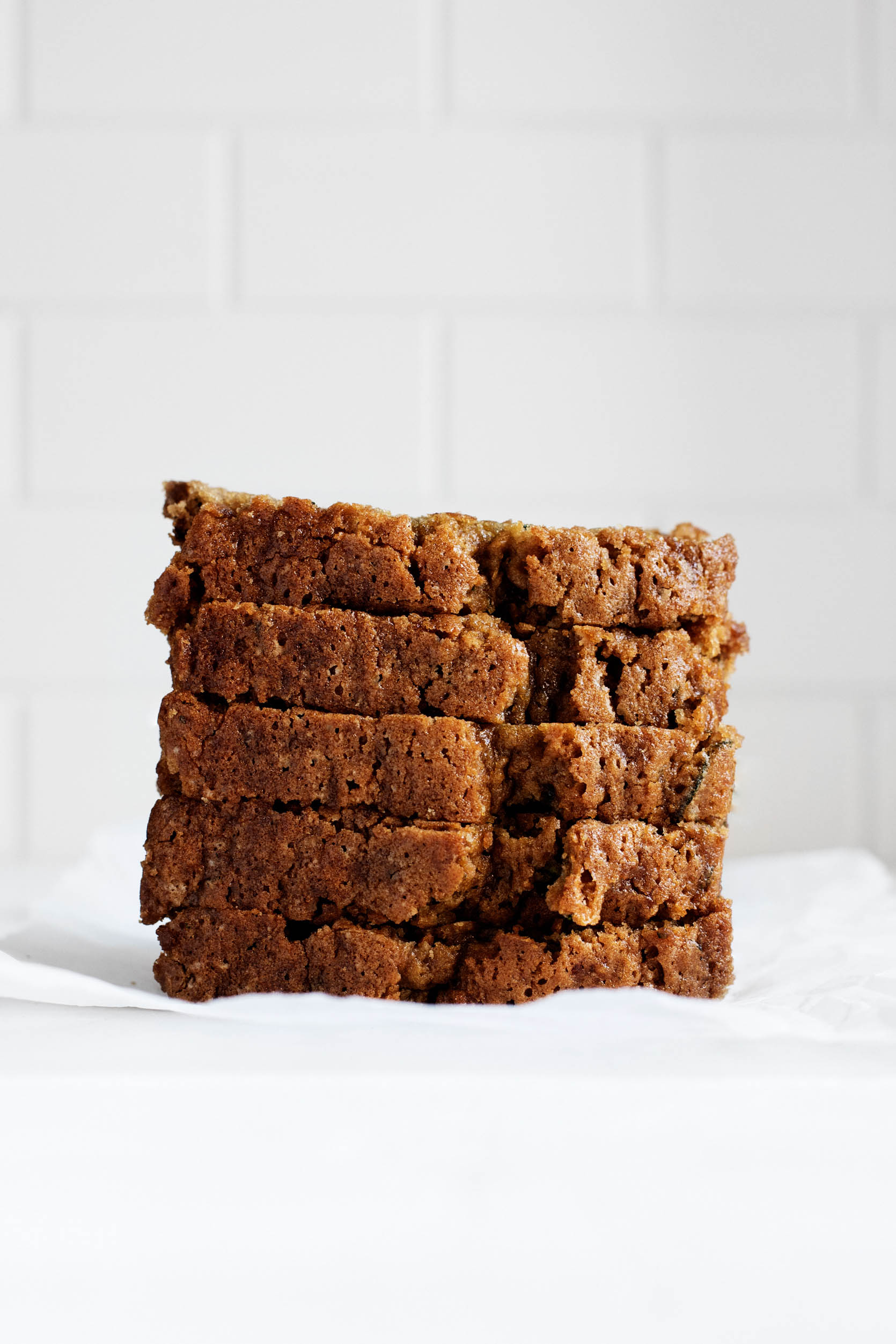 A stack of zucchini bread slices rest on a small piece of white parchment paper.