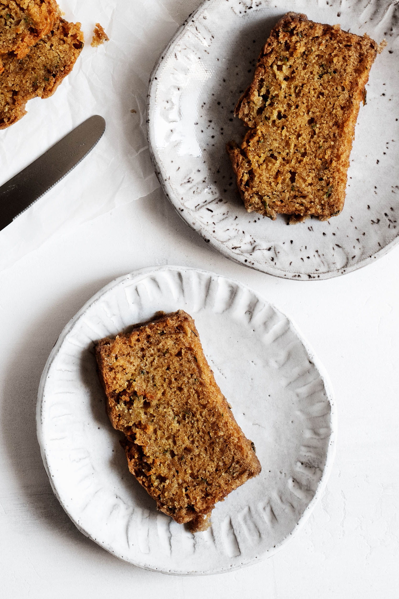 Two slices of a vegan quick bread rest on ceramic dessert plates. A cutting knife is pictured nearby.