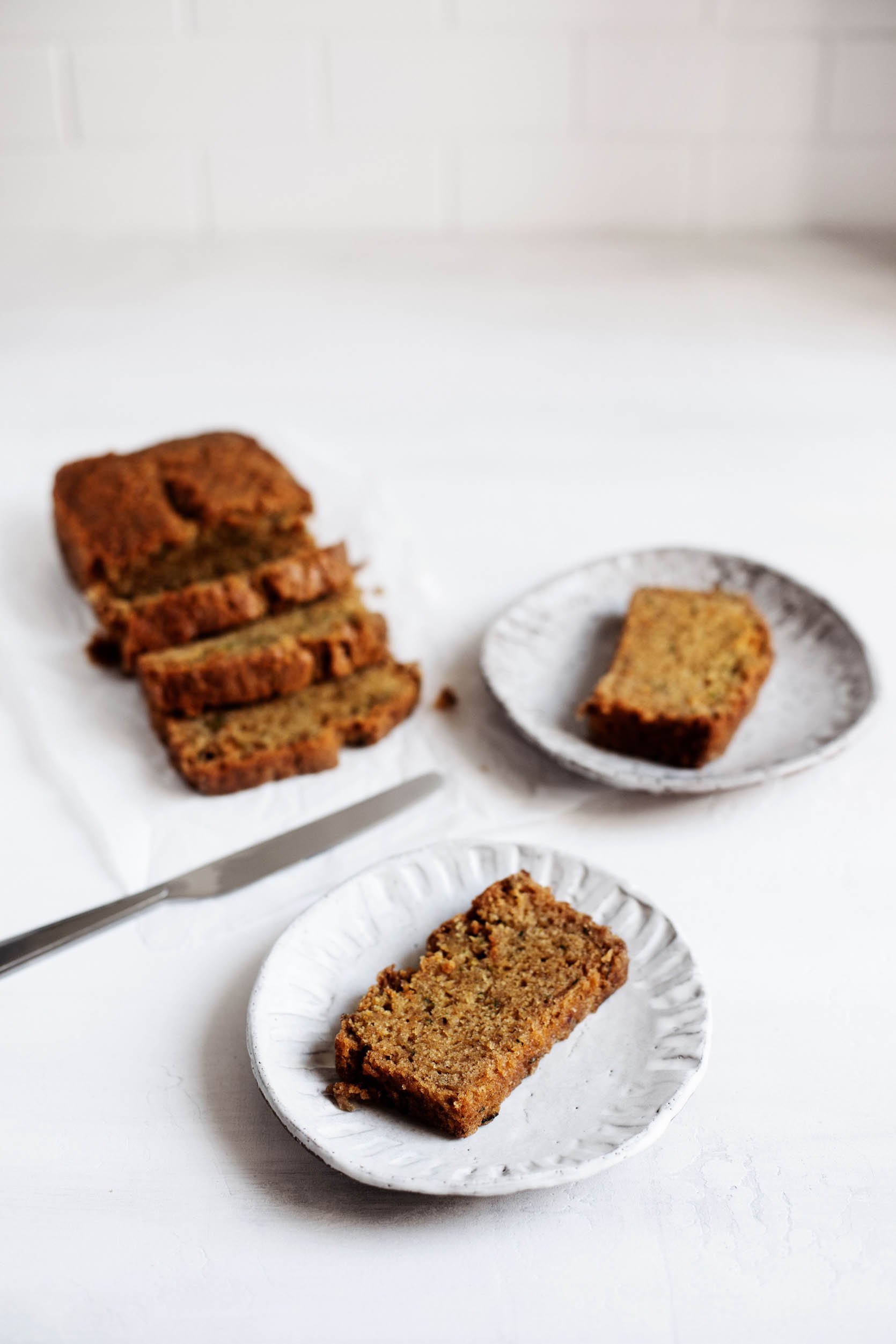 Vegan zucchini bread has just been sliced into pieces, with a knife that's pictured nearby. The slices are served on small, ceramic plates.