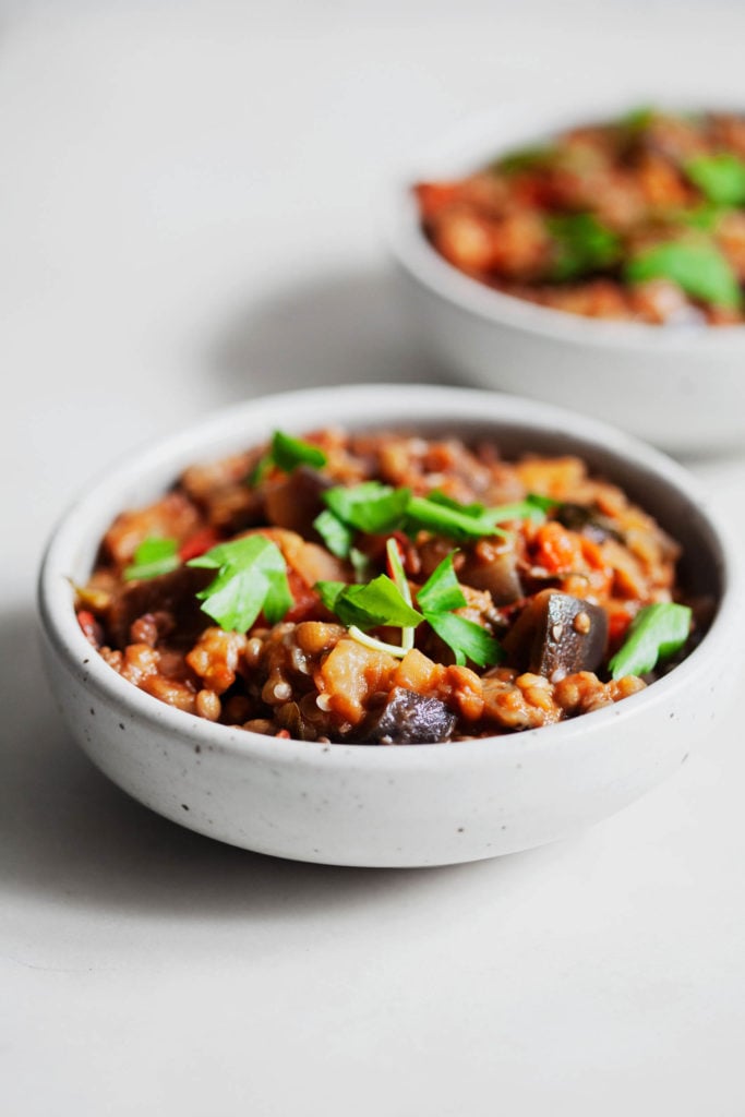 A bright, sideways shot of stewed eggplant tomato lentils and herbs.