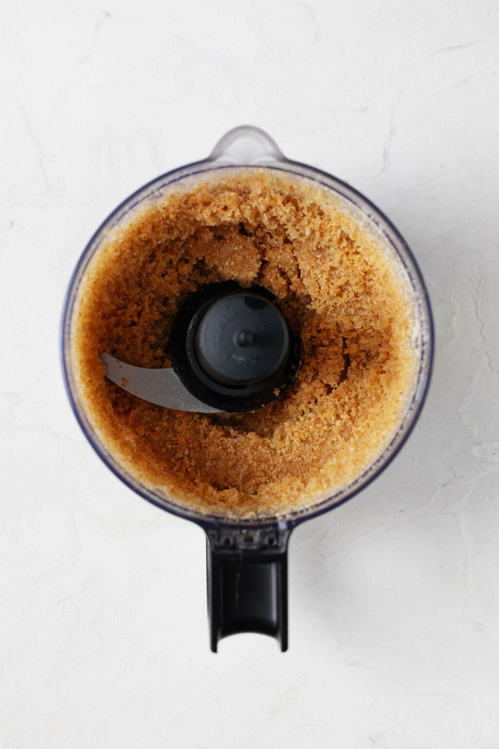 An overhead image of a food processor, which is being used to make a crumbly graham cracker crust.