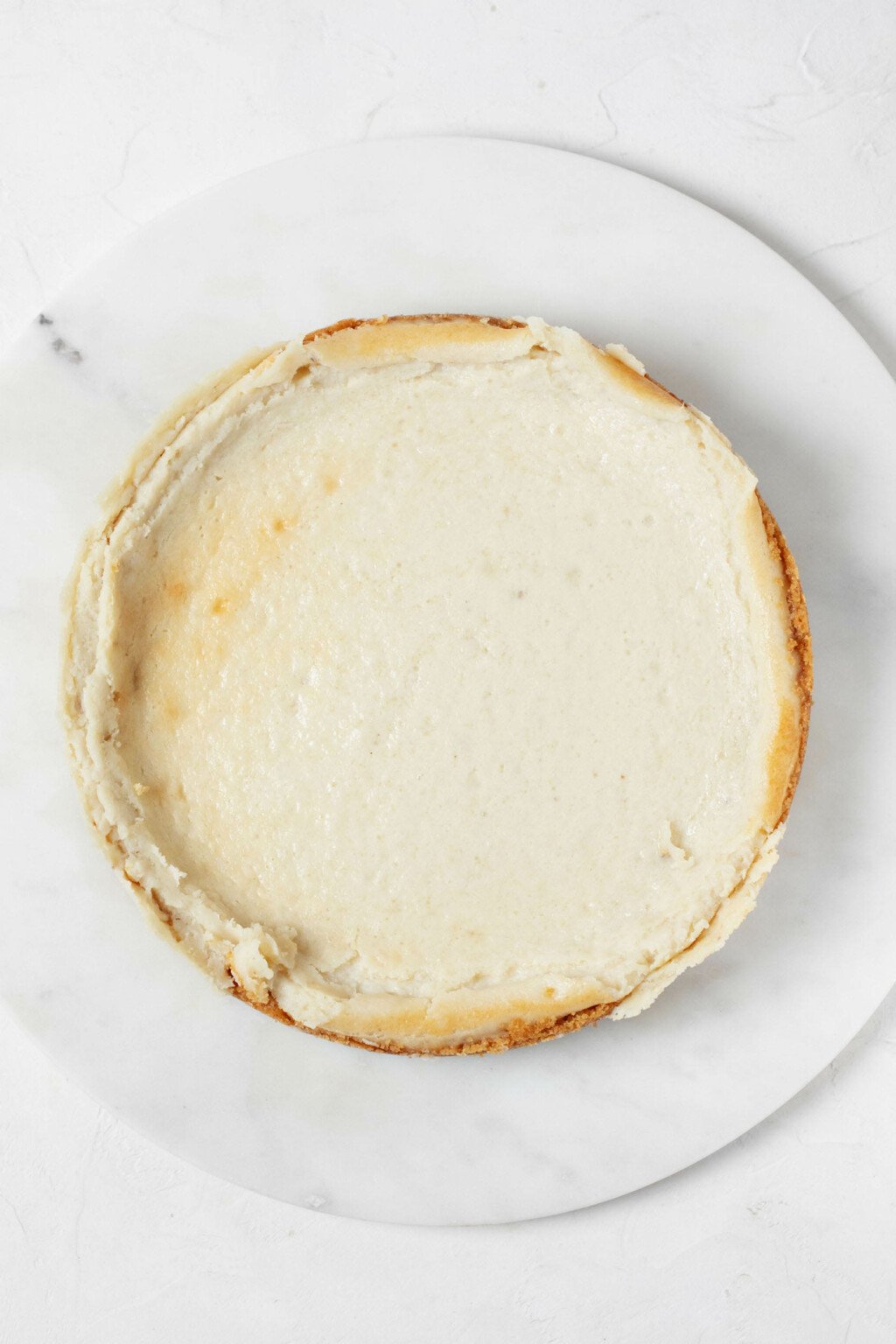 A round, white platter holds a freshly baked vegan cheesecake.