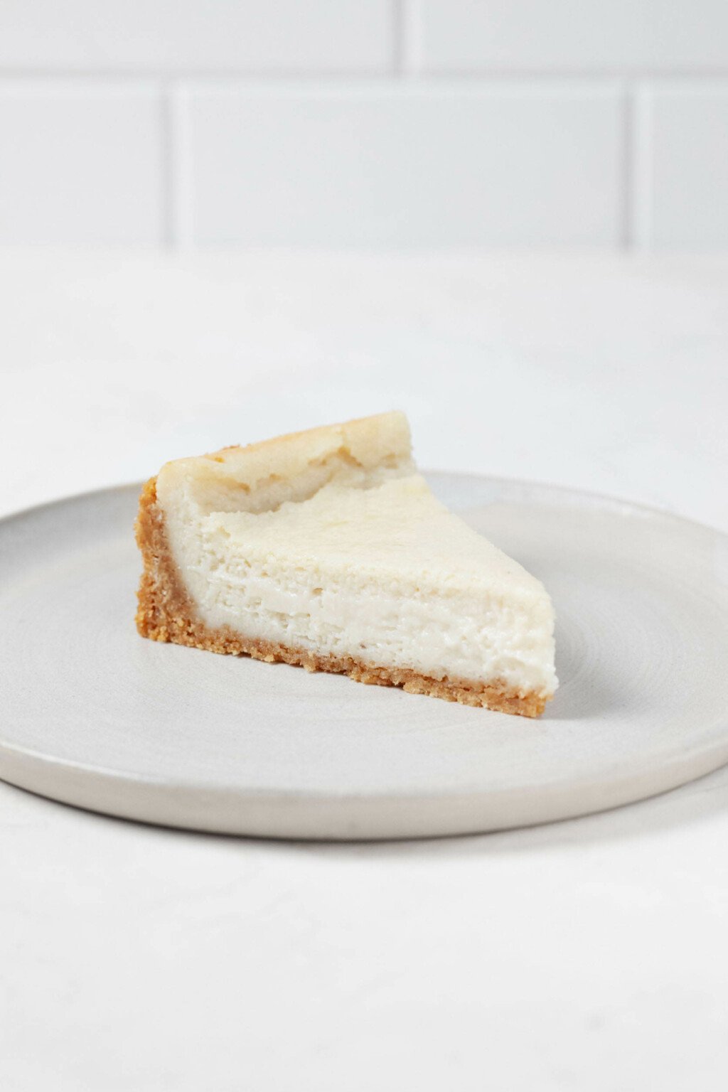 A slice of ultra creamy vegan cheesecake is resting on a round plate.