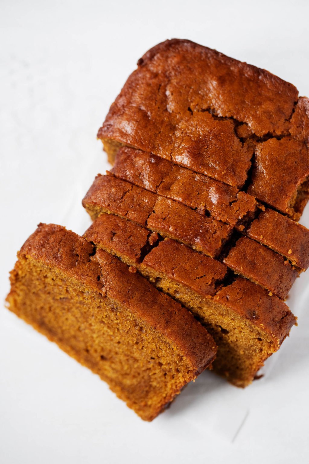 A loaf of classic vegan pumpkin bread, partially sliced and golden brown on top.