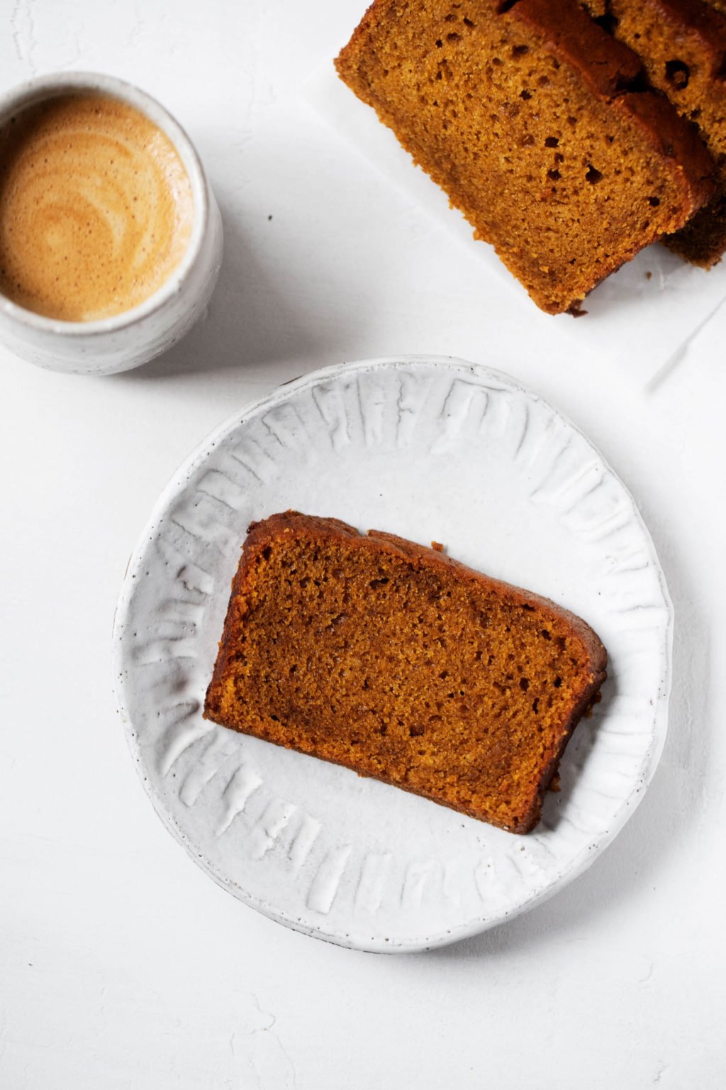 An overhead shot of a slice of vegan pumpkin bread, served with a warm latte.