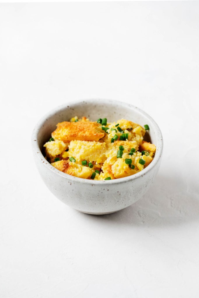 A side angle shot of a small serving of golden corn pudding, topped with snipped chives.