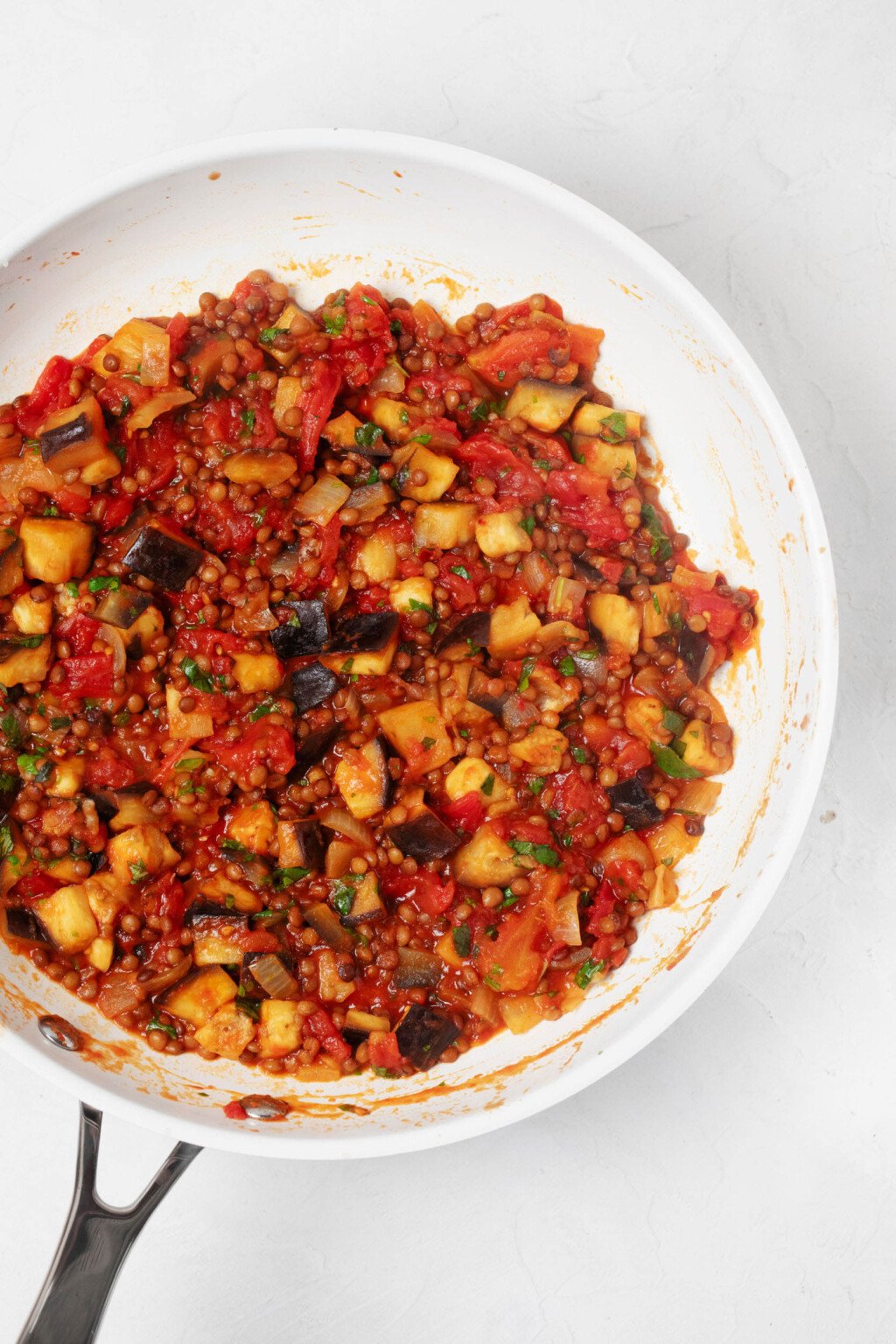 An overhead image of a white skillet, which is being used to stew a lentil and eggplant mixture.