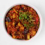 An overhead image of stewed tomatoes, eggplant, and lentils, topped with chiffonade of fresh green herbs.