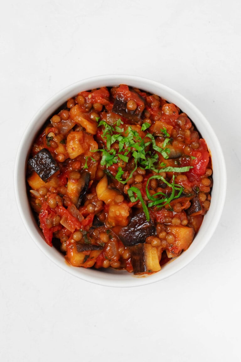 An overhead image of stewed tomatoes, eggplant, and lentils, topped with chiffonade of fresh green herbs.