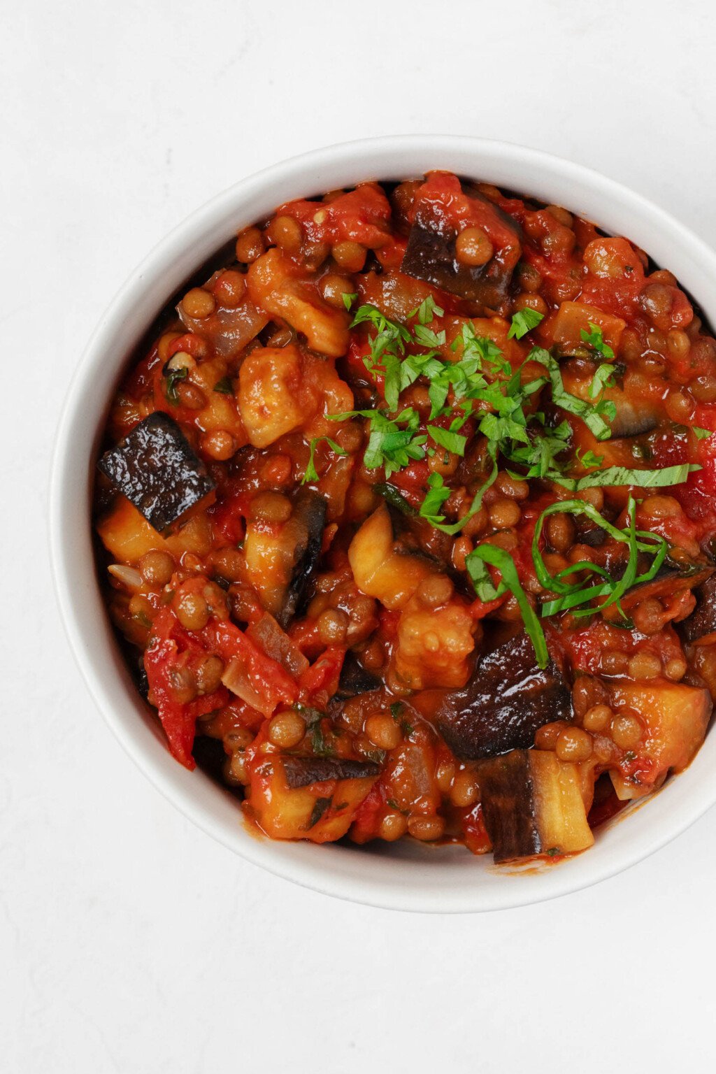 An overhead image of stewed tomatoes, eggplant, and lentils, topped with chiffonade of fresh green herbs.