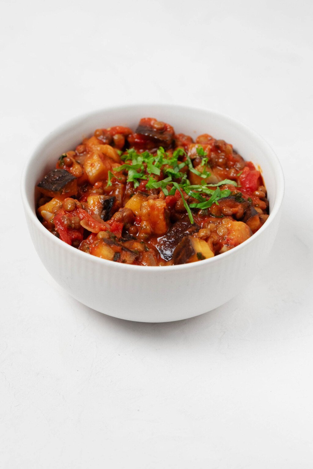 An overhead image of stewed tomatoes, eggplant, and lentils, topped with chiffonade of fresh green herbs.