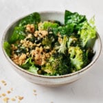 An angled shot of a vegan crispy broccoli Caesar salad, with fresh bread crumbs scattered over the marble surface.