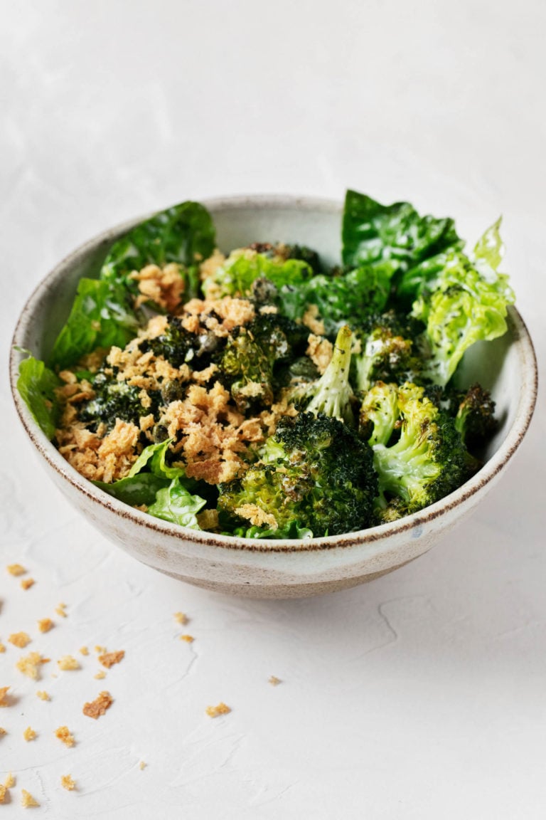 An angled shot of a vegan crispy broccoli Caesar salad, with fresh bread crumbs scattered over the marble surface.