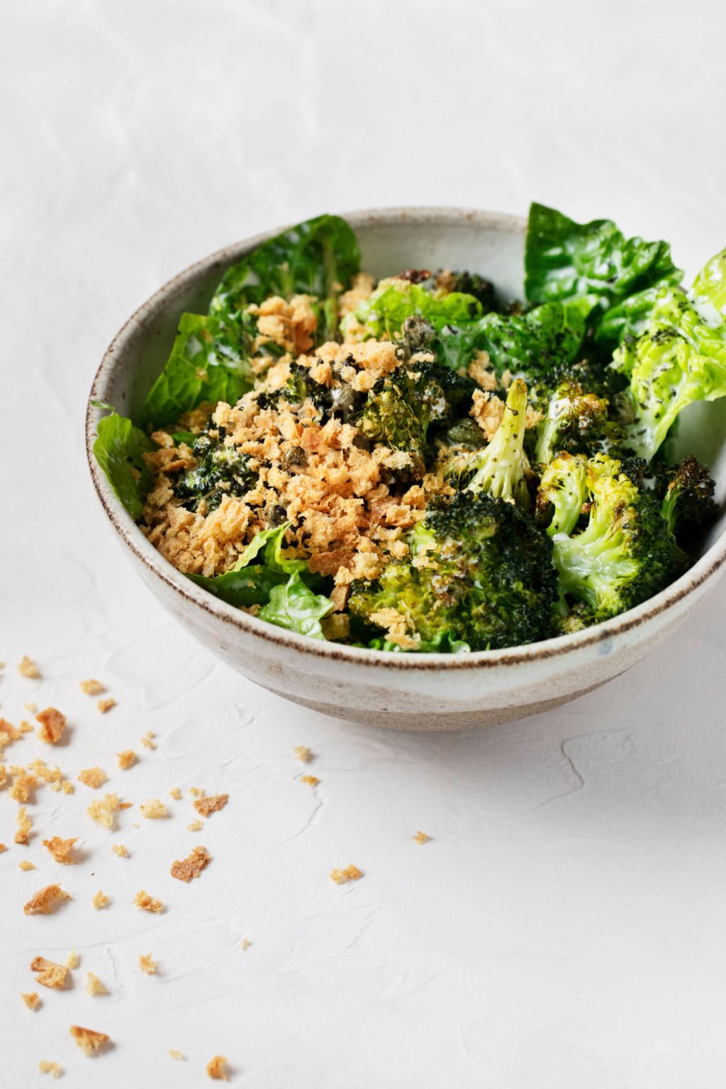 An angled photograph of a vegan Caesar salad, accompanied by a sprinkle of fresh bread crumbs.