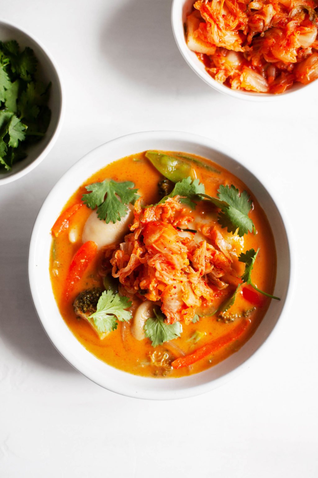 A bowl of red curry soup, garnished with a generous scoop of kimchi.