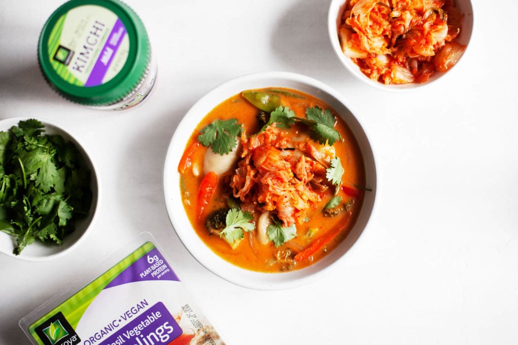 A bowl of red curry soup with Nasoya dumplings and kimchi and fresh cilantro on the side.