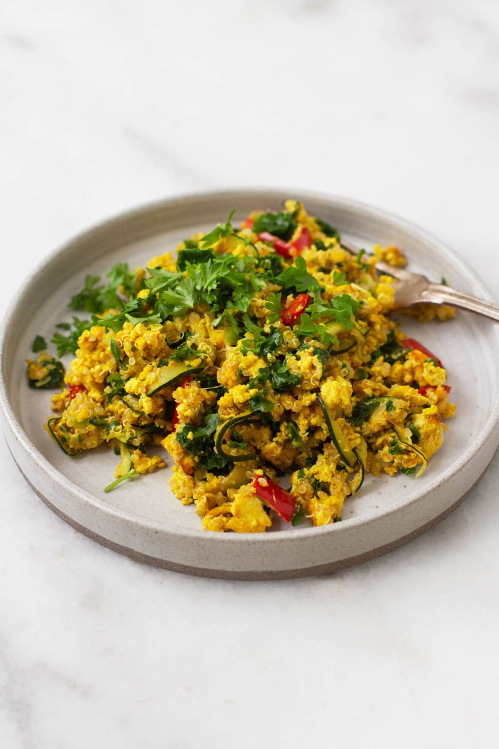 A vibrant, colorful plate of vegan tofu vegetable scramble with quinoa folded in. Topped with fresh, chopped herbs.