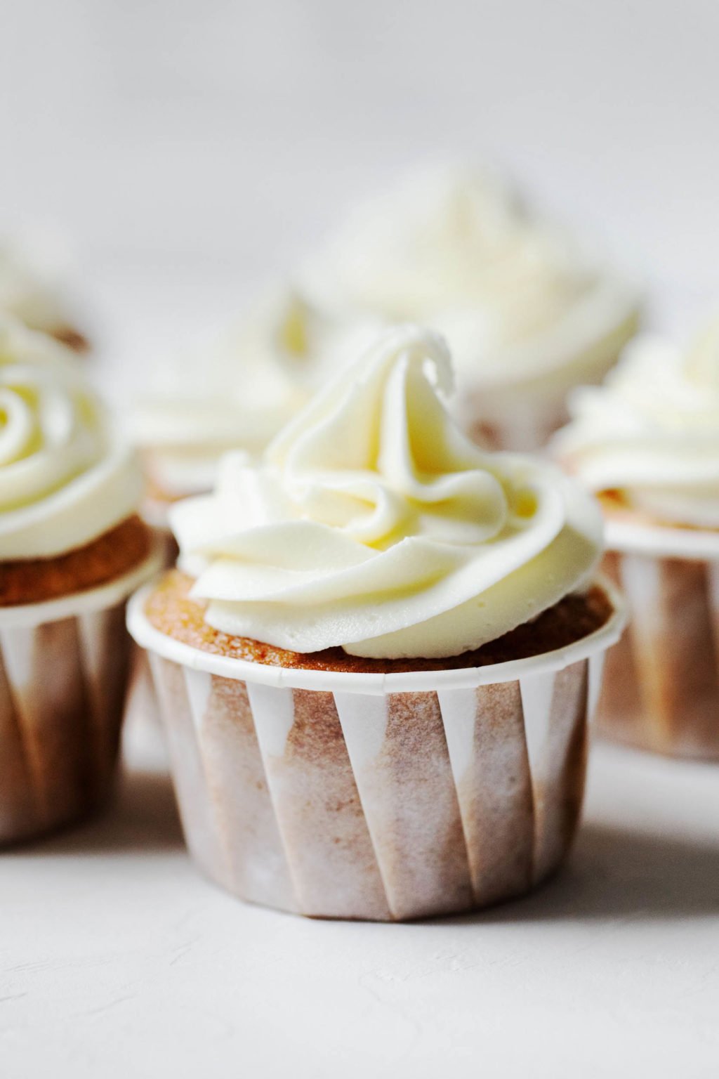 An angled photograph of vegan apple cider cupcakes, each with swirls of vegan cream cheese frosting.