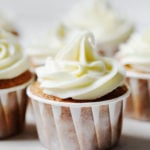 An angled photograph of vegan apple cider cupcakes, each with swirls of vegan cream cheese frosting.