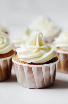 An angled photograph of vegan apple cider cupcakes, each with swirls of vegan cream cheese frosting.