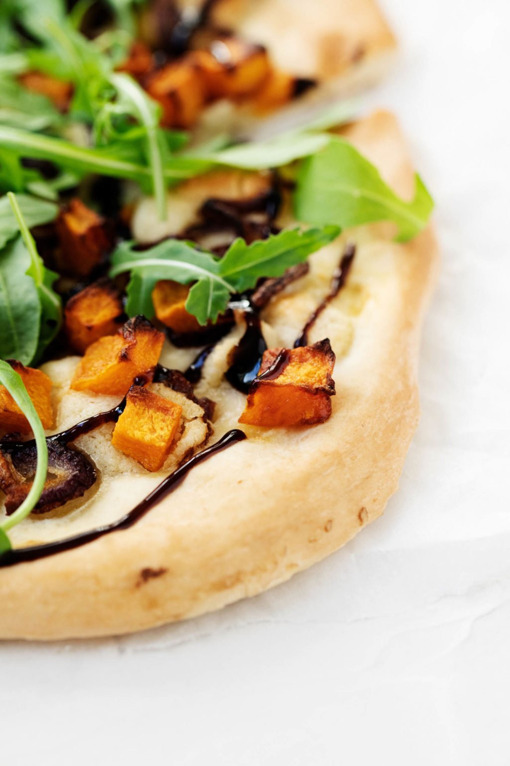 Zoomed in on an autumnal vegan pizza, made with roasted butternut squash, caramelized red onion, and arugula.