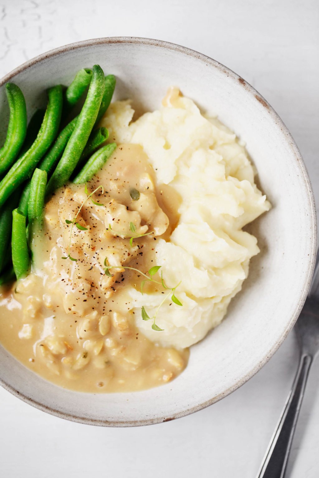 A close up of vegan mashed potatoes, topped with festive tempeh and gravy and a side of green beans.