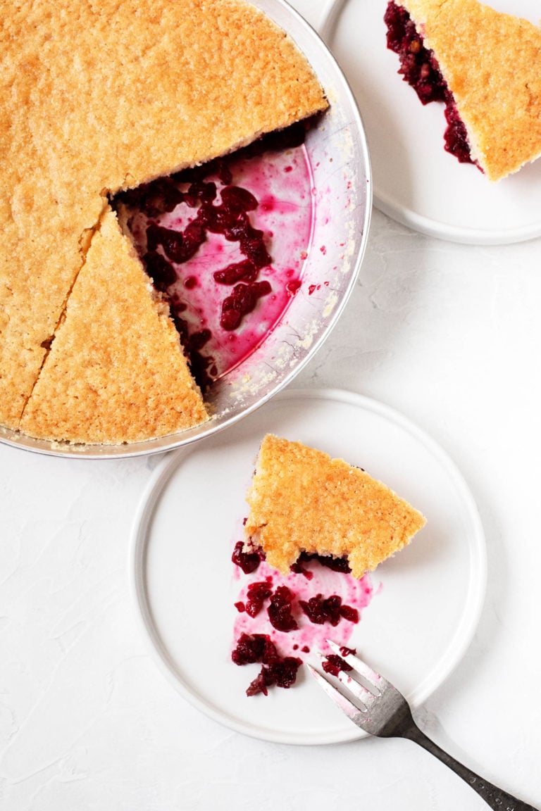 A slice of cranberry "Nantucket pie," which is really a vanilla cake poured over cranberries and walnuts, sits in a baking dish with a cut slice nearby.